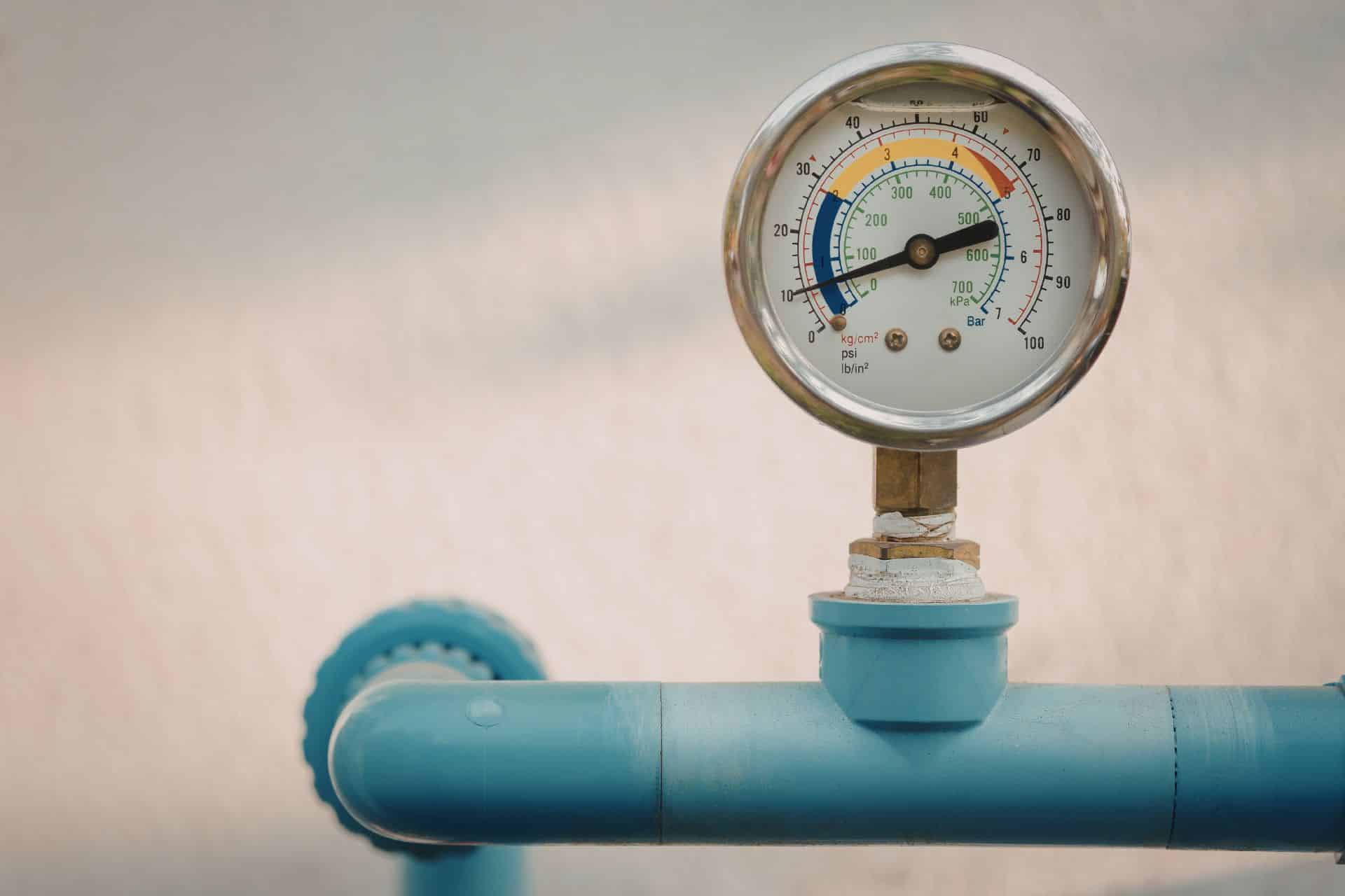 Under pressure - The Sales Vault - The Sales Vault Close-up of an analogue pressure gauge mounted on a teal pipe, showing colored bands and a black needle across the dial in an industrial setting