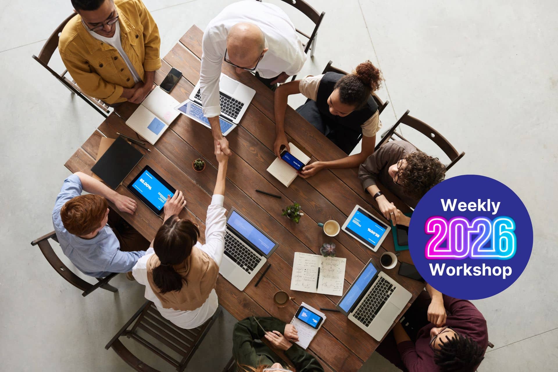 Overhead view of a diverse team around a wooden table with laptops and tablets, shaking hands; a large blue circle reads 'Weekly 2026 Workshop' in the corner.