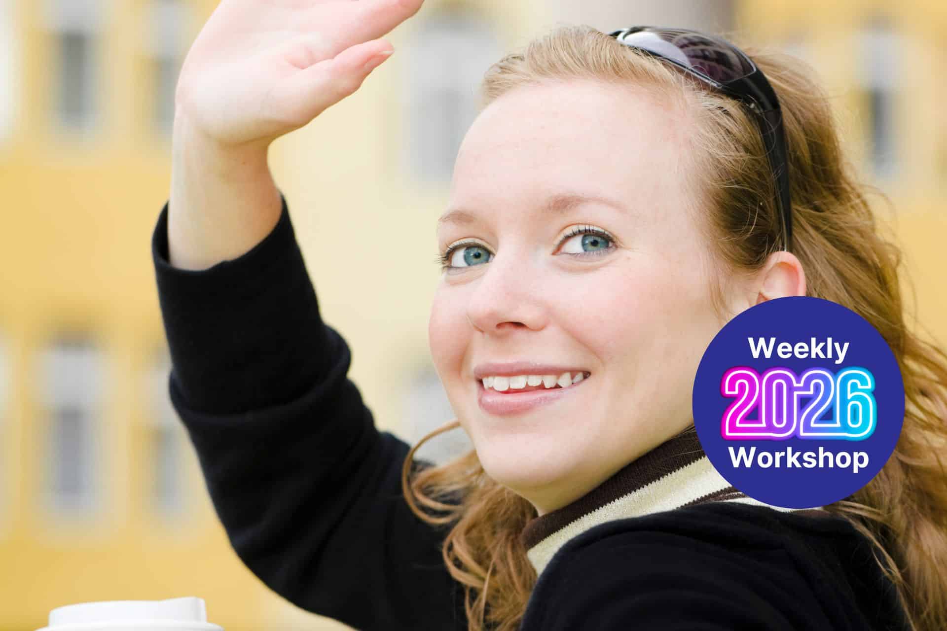 Smiling woman waving at the camera with a circular badge reading 'Weekly 2026 Workshop' on her chest/shoulder area