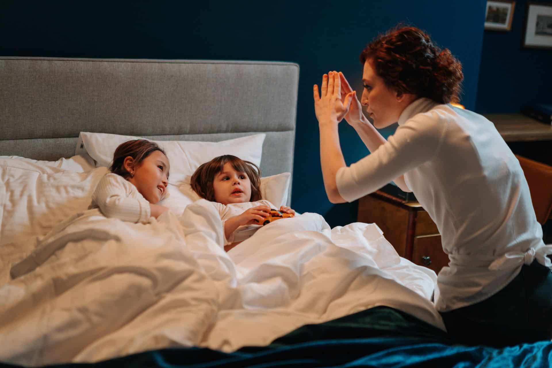tell the story - The Sales Vault - The Sales Vault Parent leans over bed, high-fiving two children tucked in under white blankets in a cozy bedroom.