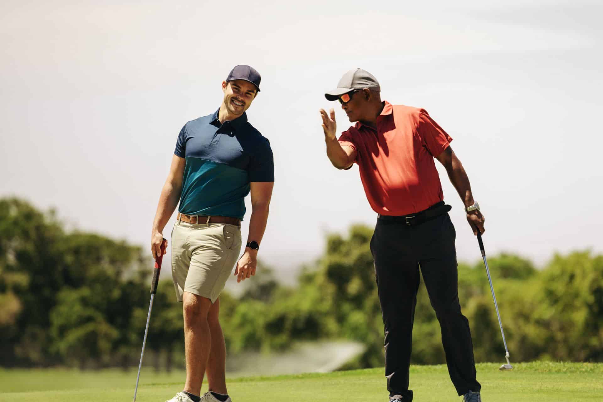Listen to yourself blog - The Sales Vault - The Sales Vault Two male golfers on a sunny golf course, one in a blue polo and beige shorts, the other in a red polo and dark pants with clubs in hand.