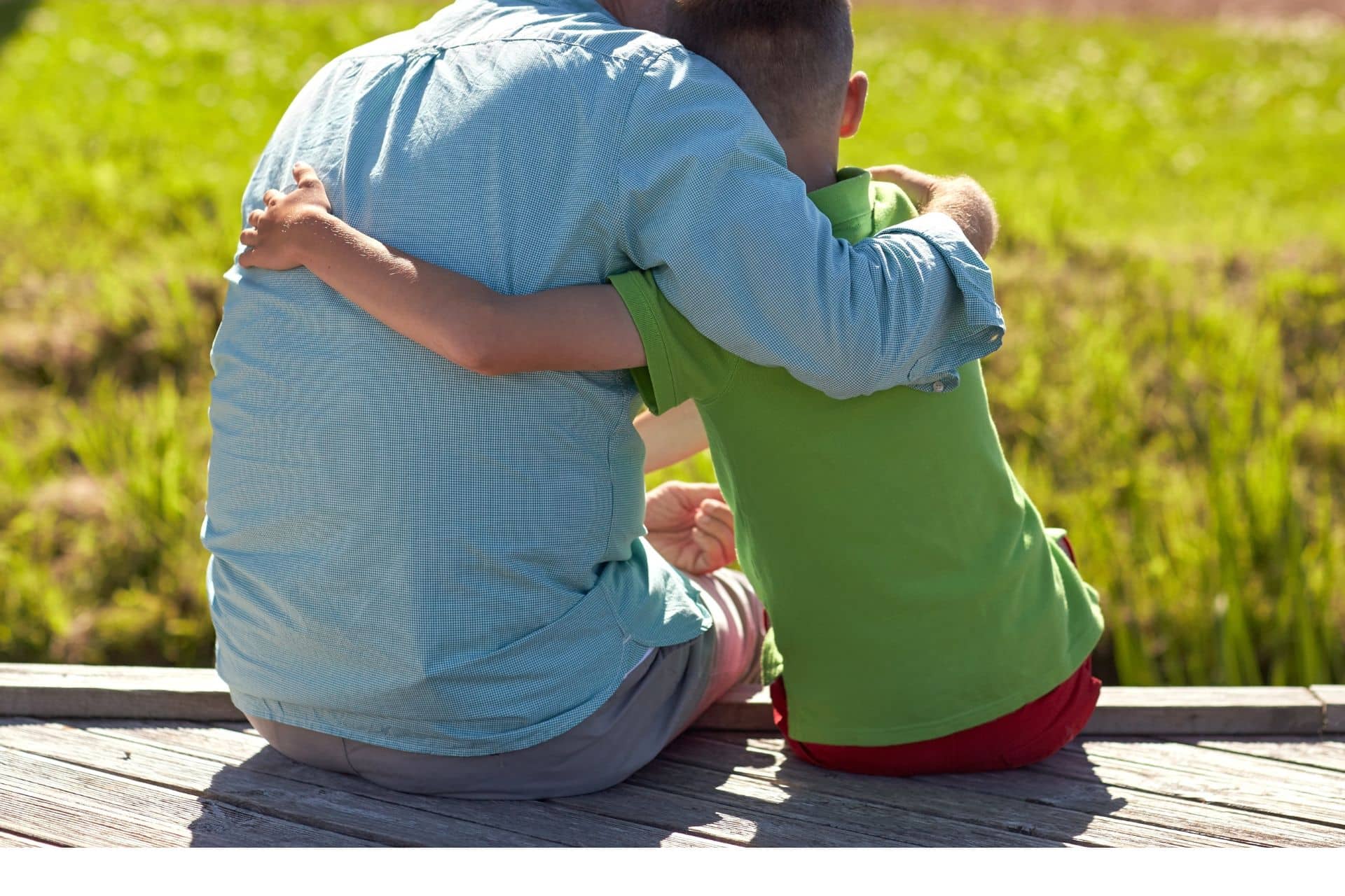 bestie - The Sales Vault - The Sales Vault Two people sitting on a wooden deck outdoors, arms around each other in a hug, with a green field in the background.