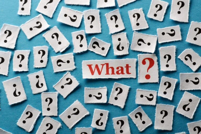Cluster of torn white cards with black question marks scattered on a blue background, with a central card reading “What?”